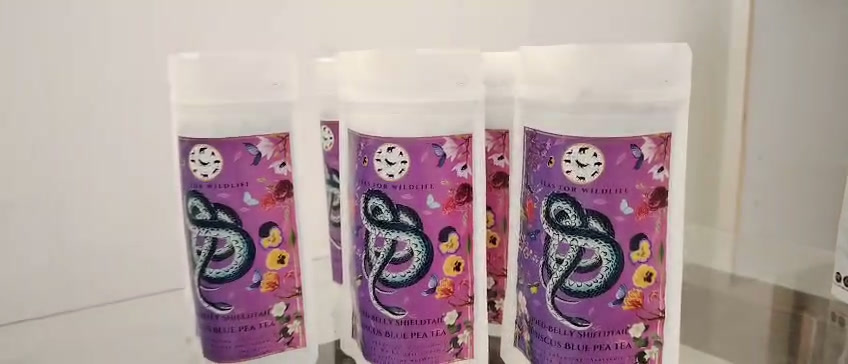 Three sealed pouches of Hibiscus Blue Pea Tea lined up on a shelf, purple snake labels facing forward.