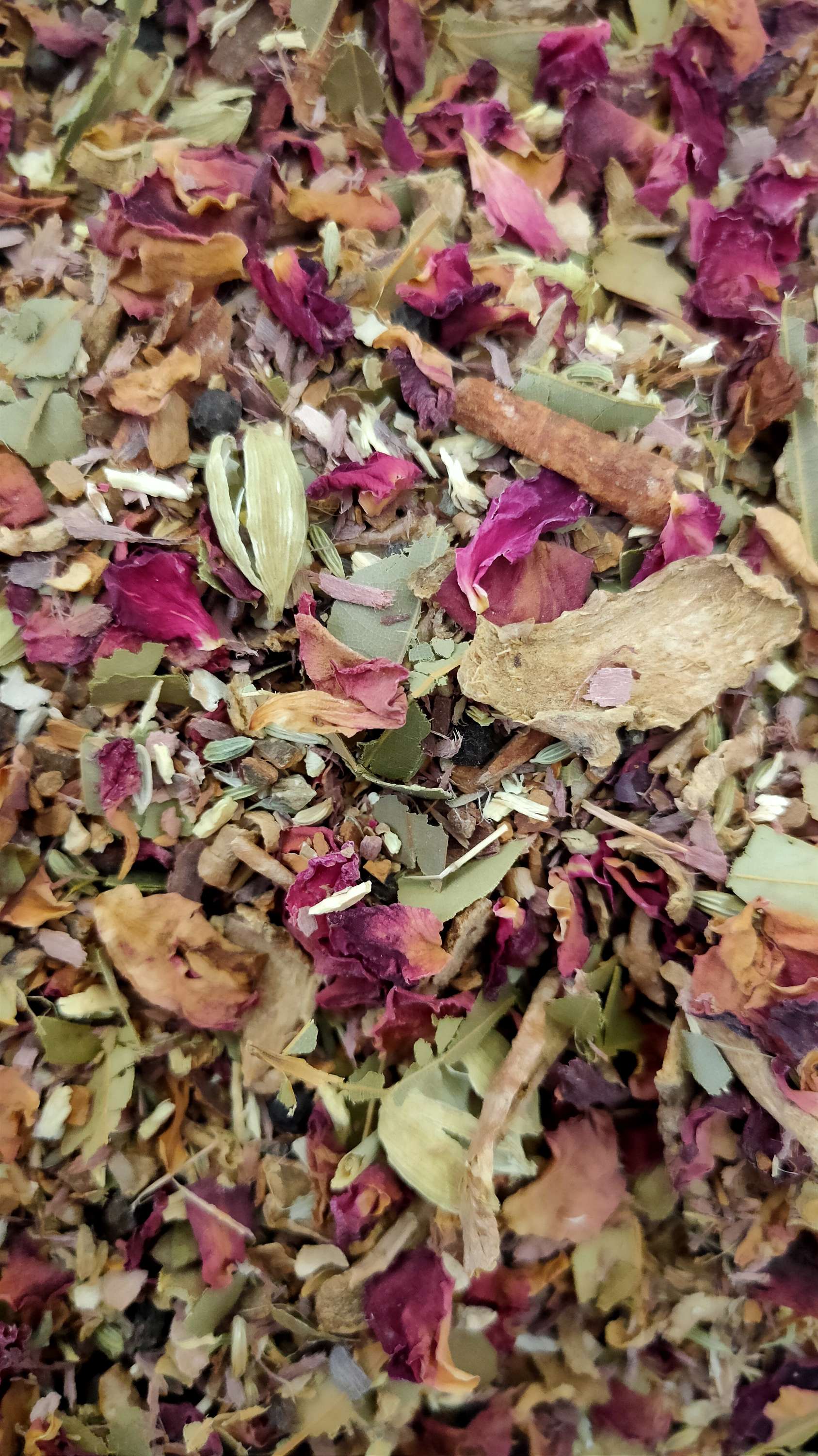 Loose-leaf Arjun Cinnamon blend close-up: crimson rose petals, green leaves, cinnamon bark and dried ginger pieces