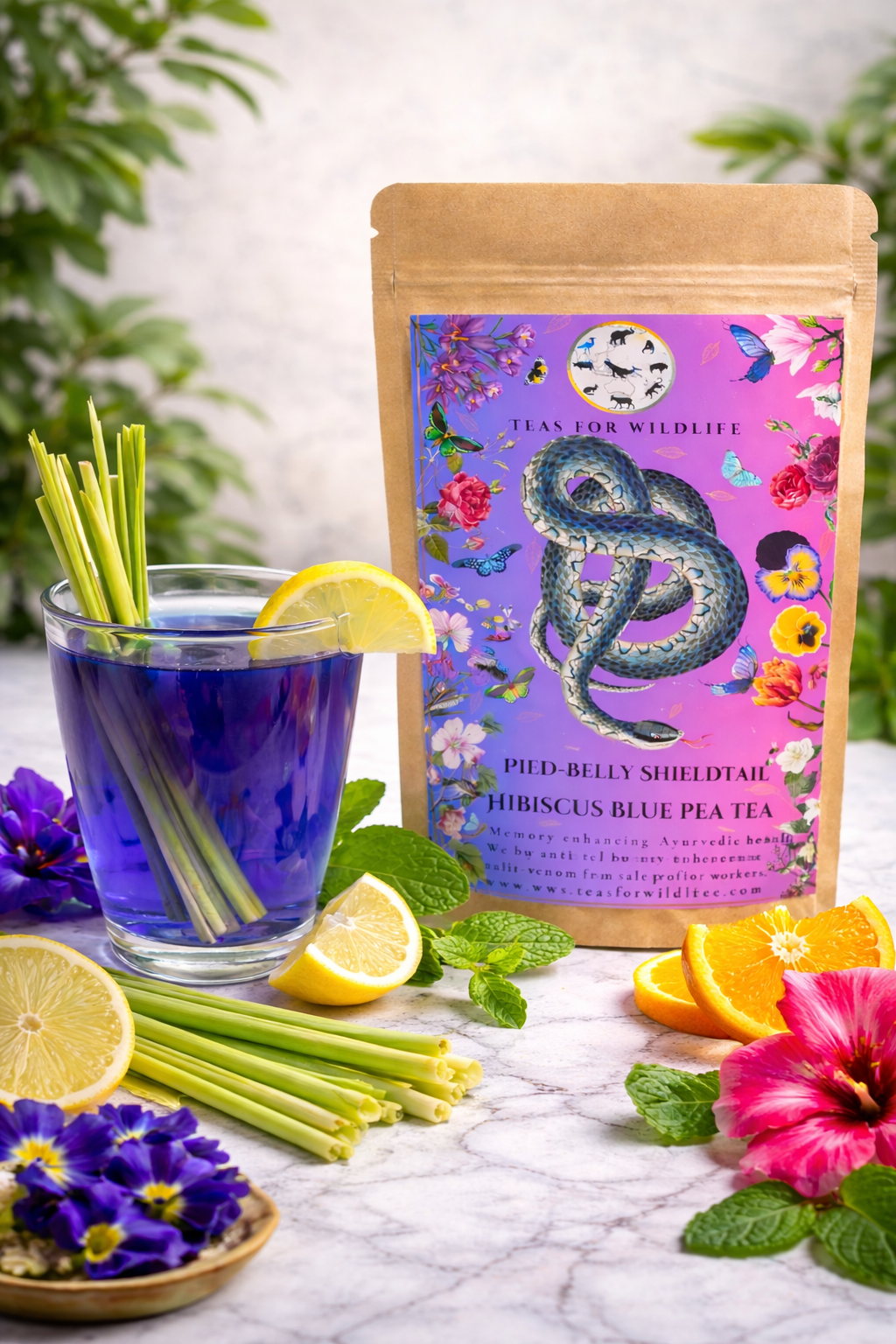 Kraft pouch with the purple snake label beside a glass of blue pea infusion, lemongrass, citrus slices, mint and hibiscus.