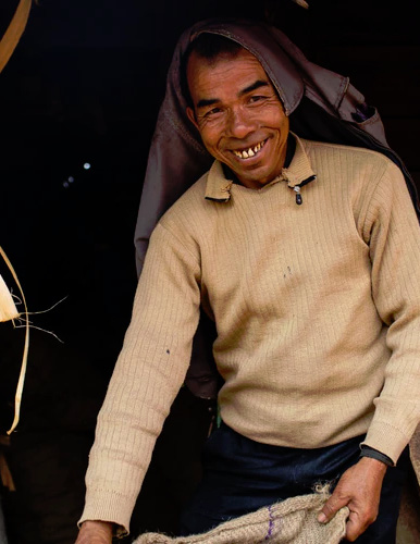 Smiling farmer in a beige sweater and head cloth standing in a dark doorway, holding a jute sack