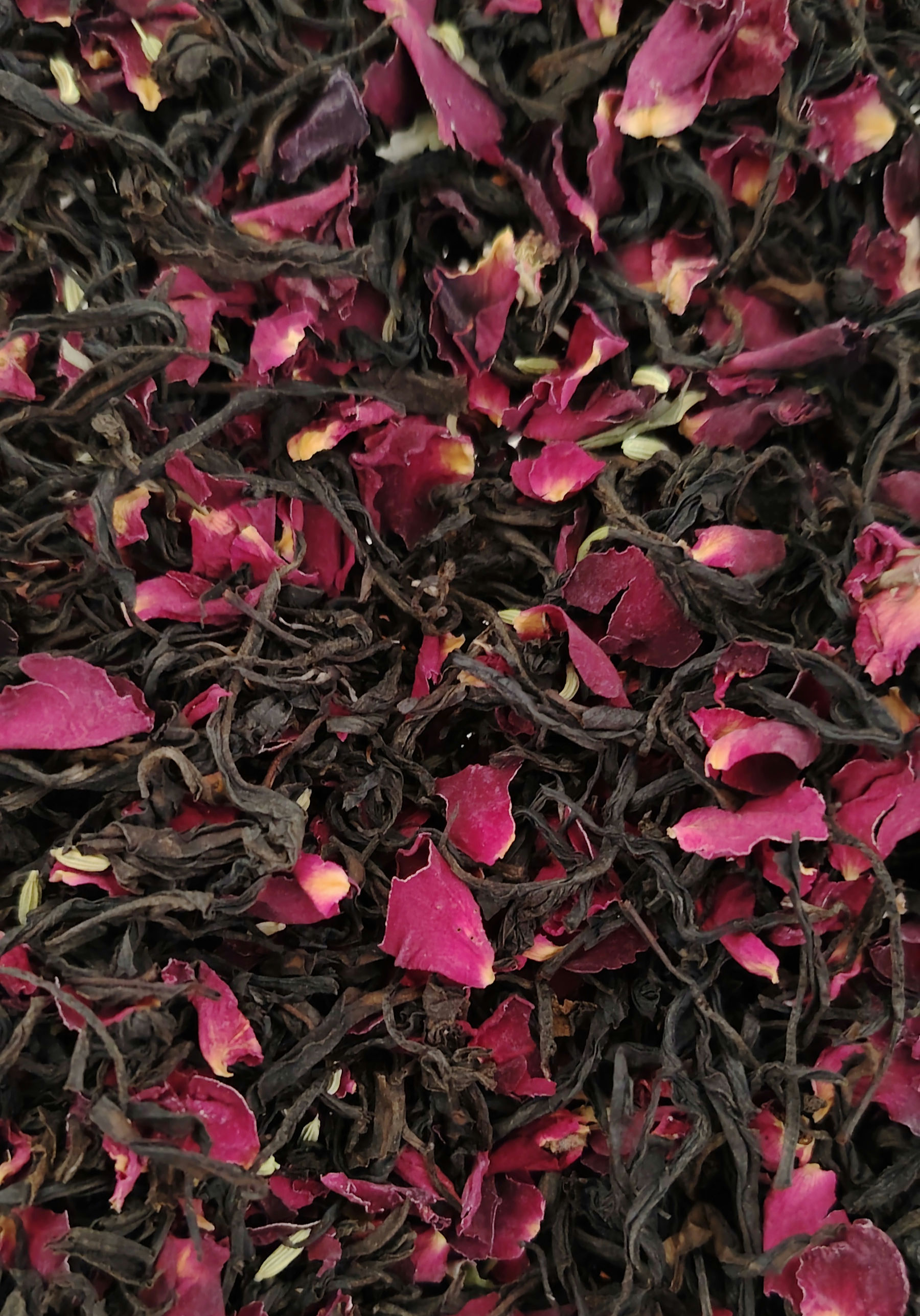 Close-up of loose black tea leaves mixed through bright pink dried rose petals.