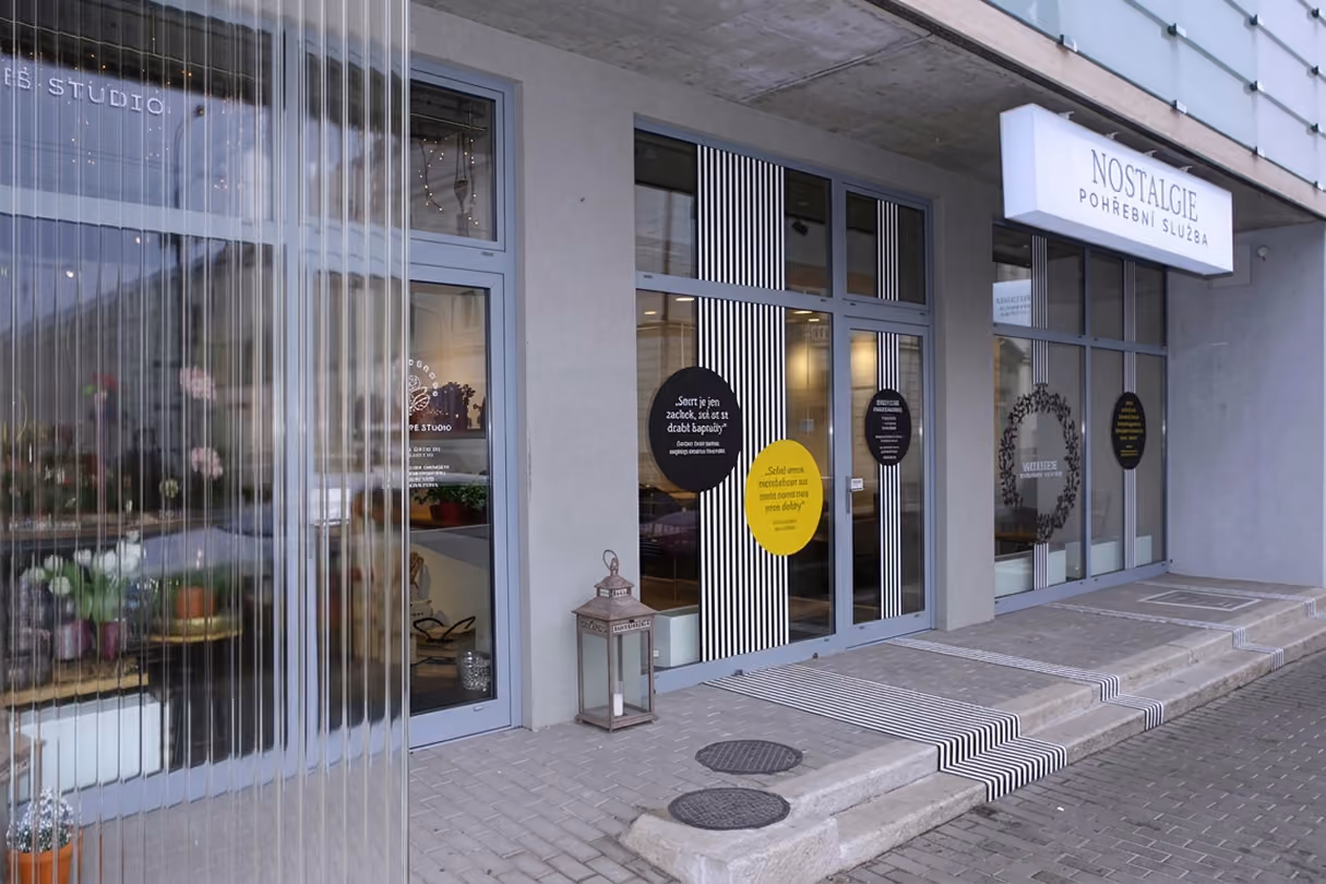 Vstup do moderní pohřební služby Nostalgie s nápisy a dekorativními pruhy na skle dveří.