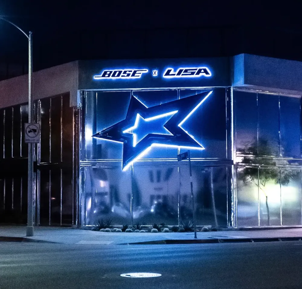 Bose x LISA storefront at night with mirror-finish facade panels, backlit logo signage, and a large blue LED-lit star