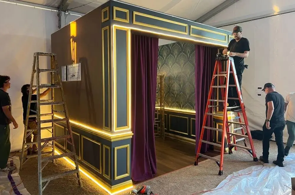 Monum Fab crew installing a lit, gold-trimmed branded room with velvet curtains and patterned wallpaper