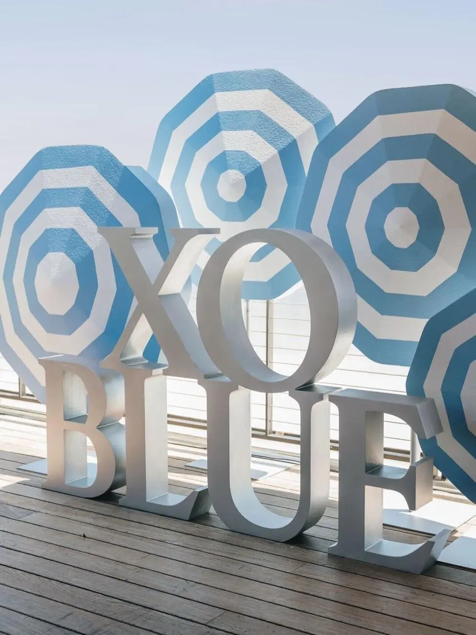 Oversized XO BLUE dimensional lettering in front of carved blue and white striped umbrella sculptures on the deck