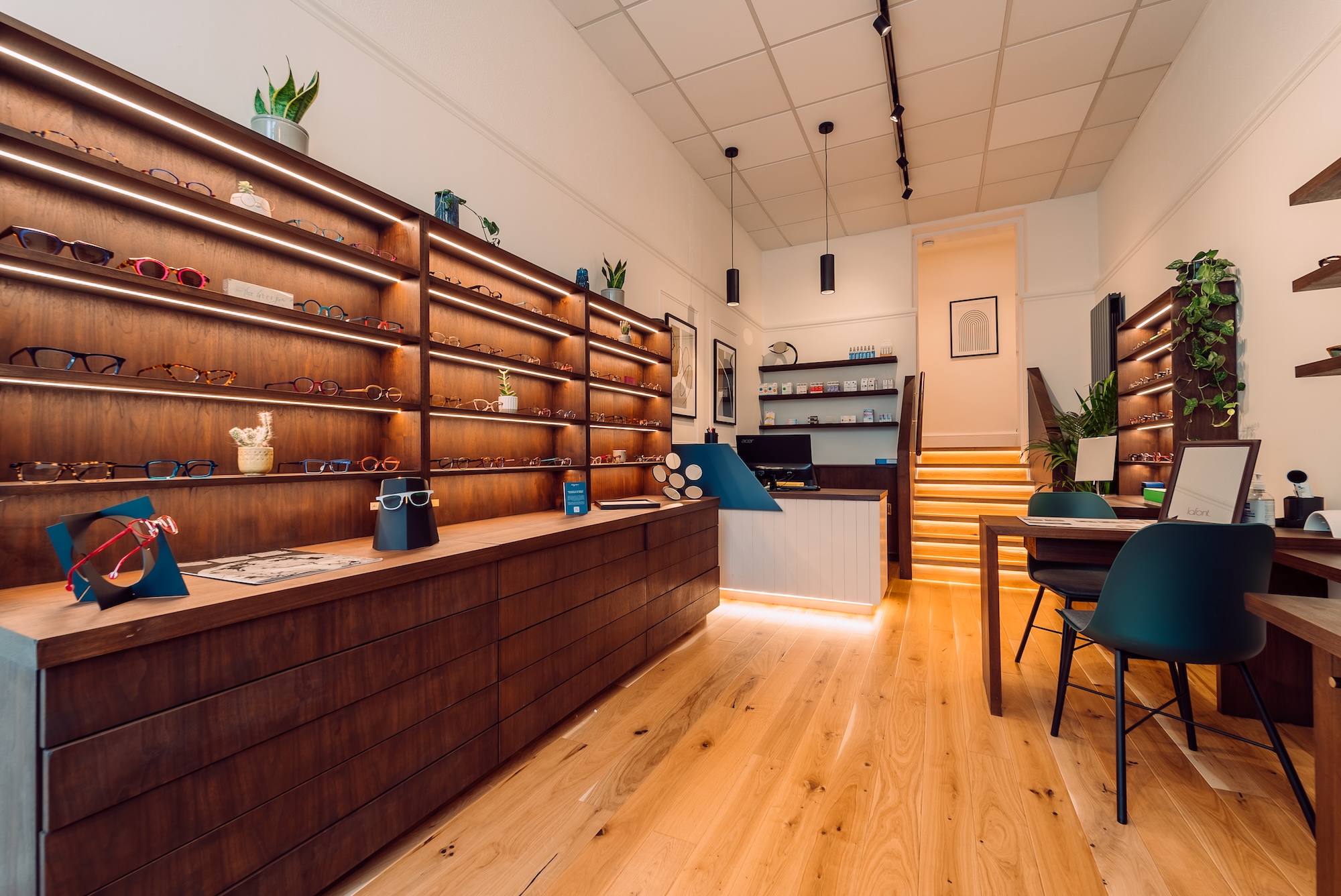 Modern eyewear store interior with wooden shelves displaying glasses and a lit staircase in the back.