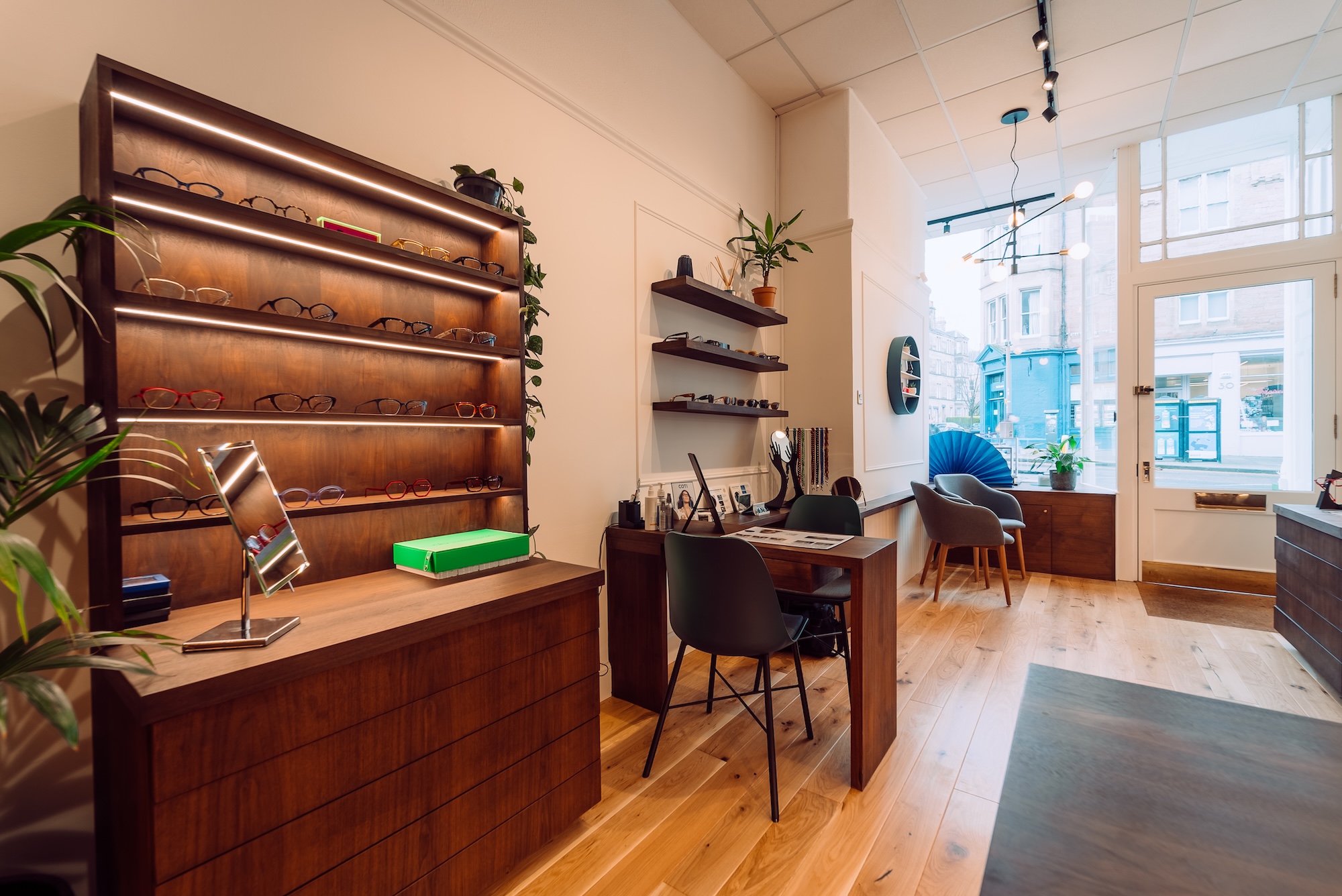 Interior of an eyewear store with wooden shelves displaying glasses and a consultation desk with chairs.