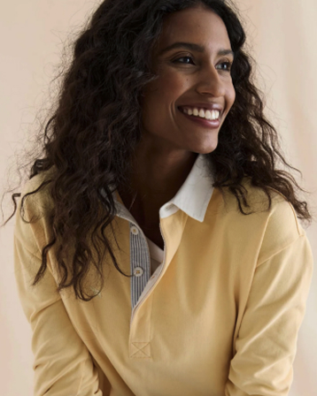 Smiling woman with curly hair wearing a yellow shirt over a white collared top.