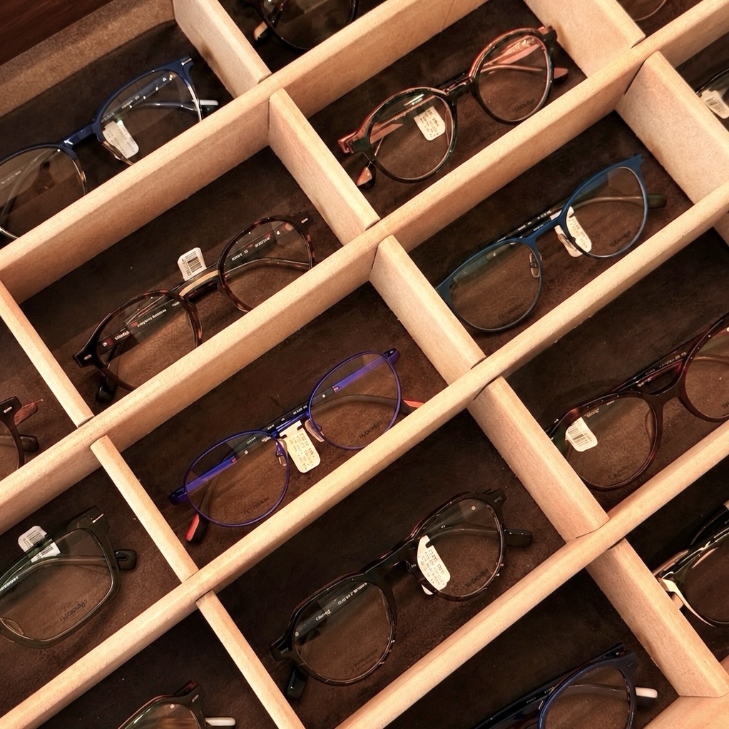 Multiple pairs of eyeglasses with various frame colors displayed in a wooden organizer tray.