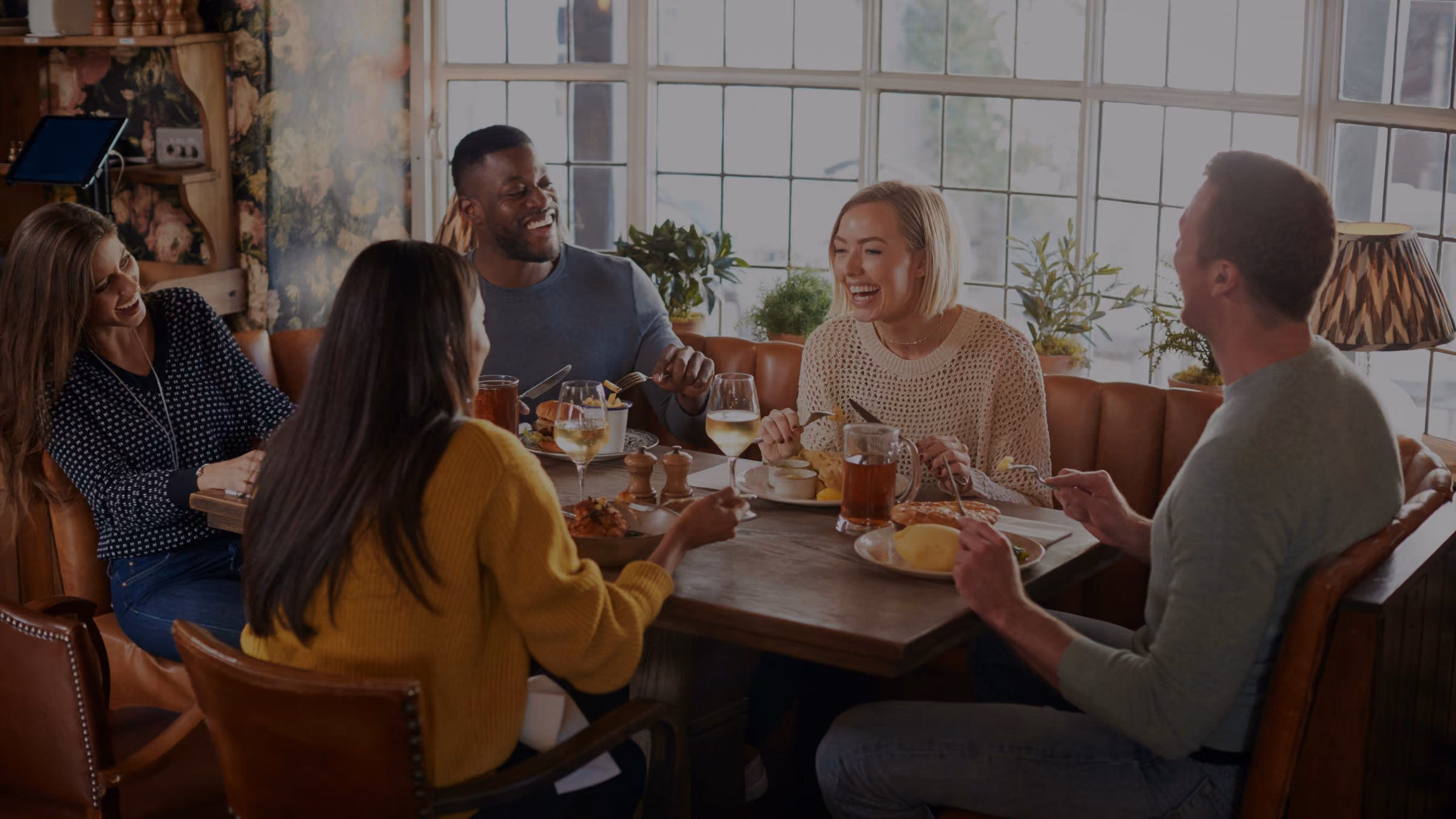 A group of friends at a warm and cosy British pub in Autumn, enjoying traditional pub food and drink while catching up and laughing together.