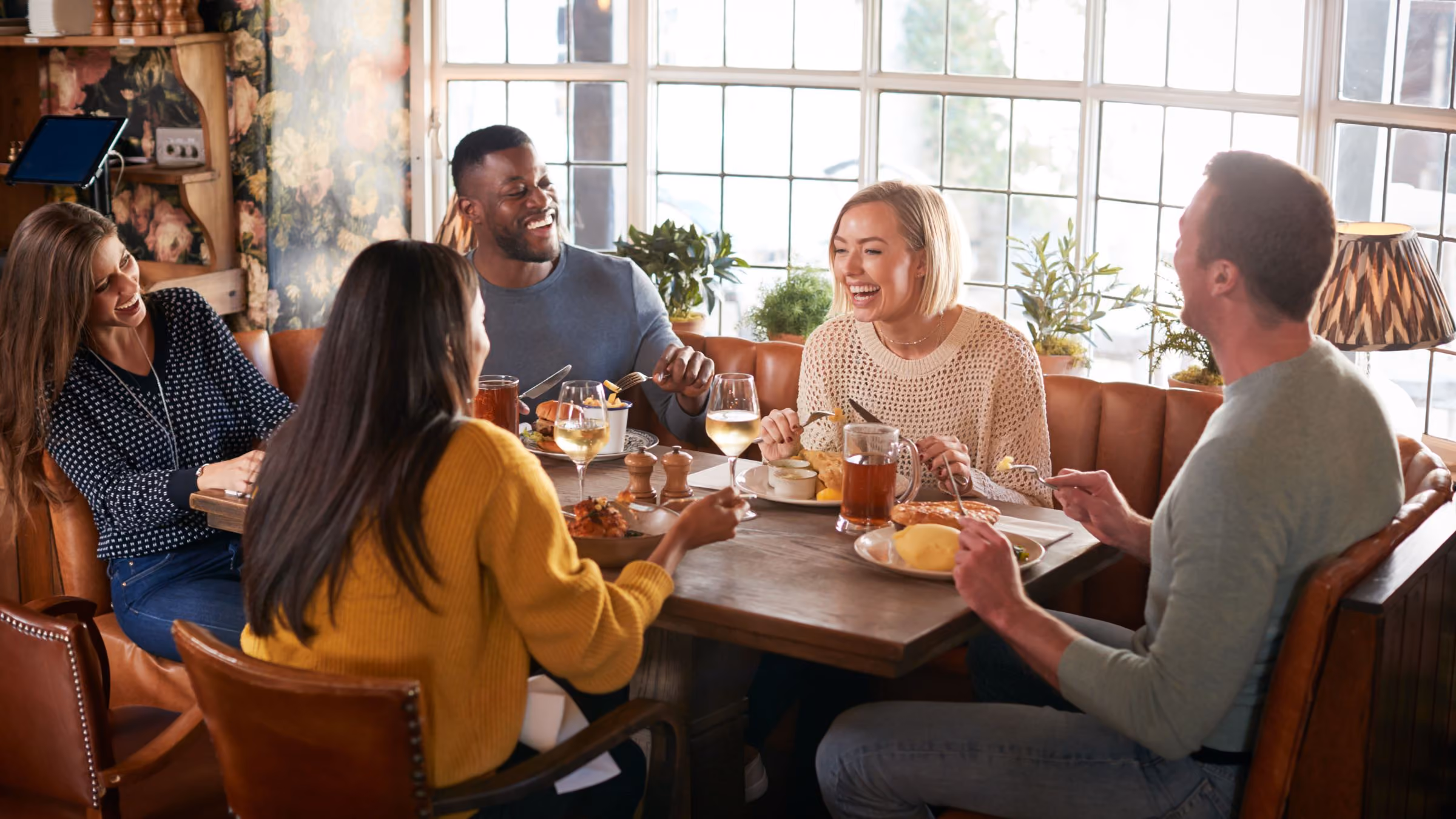 A group of friends at a warm and cosy British pub in Autumn, enjoying traditional pub food and drink while catching up and laughing together.