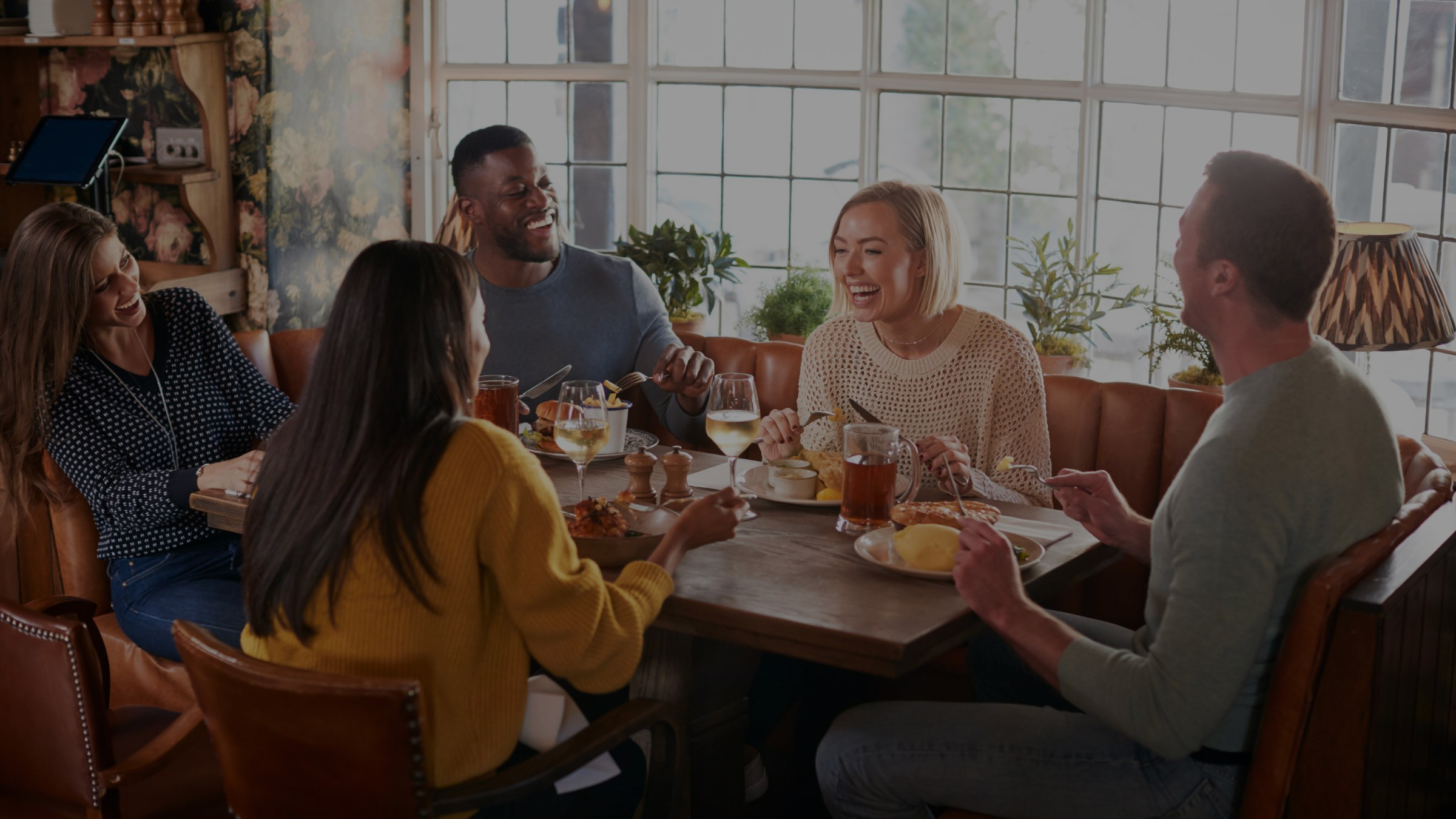 A group of friends at a warm and cosy British pub in Autumn, enjoying traditional pub food and drink while catching up and laughing together.