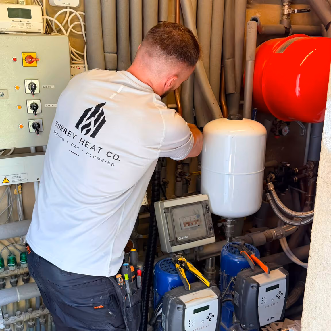 Technician from Surrey Heat Co. working on pipes and heating equipment in a utility room.