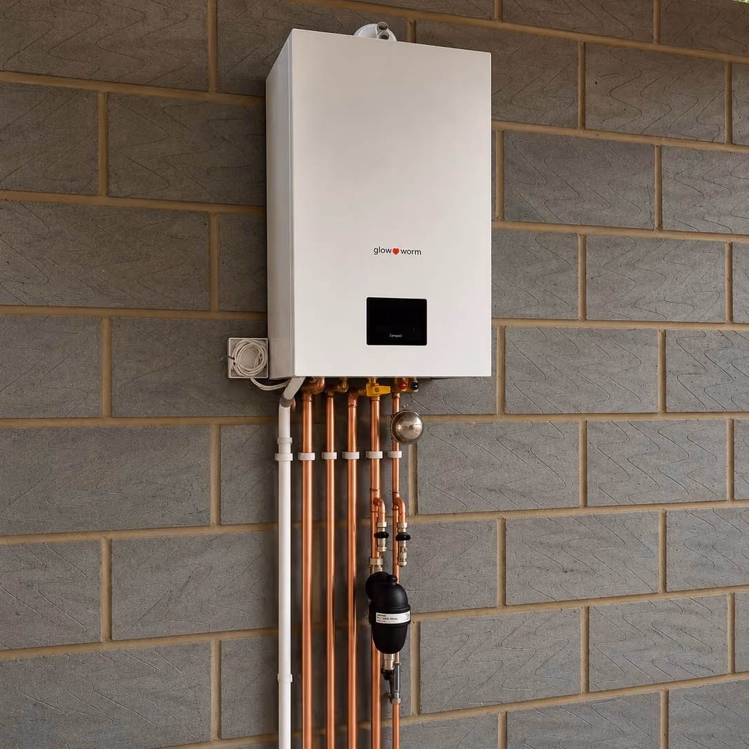 Wall-mounted Glow Worm boiler connected to six copper pipes on a gray brick wall.