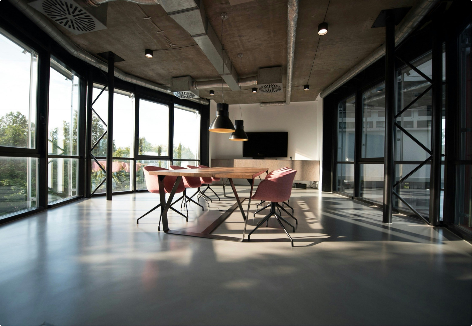 Modern conference room with wooden table, pink chairs, large windows, and a TV on the wall.
