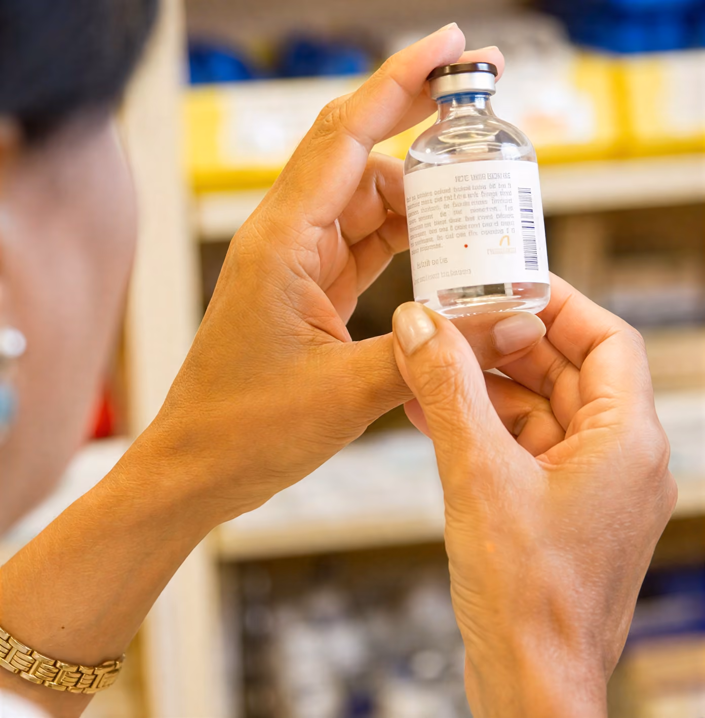 Person holding and examining a small clear medicine vial with a white label and brown cap.