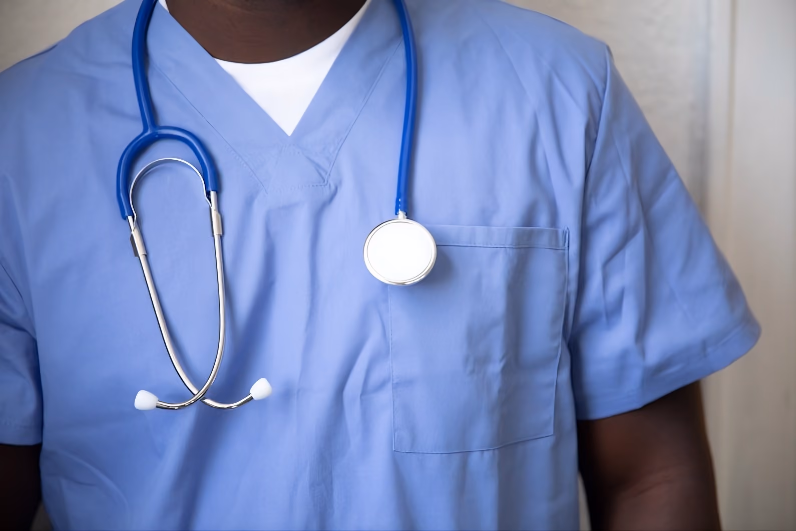 Person in blue medical scrubs wearing a blue stethoscope around their neck.