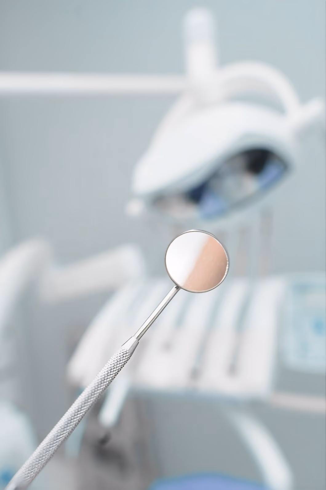Close-up of a dental mirror with blurred dental light and equipment in the background.