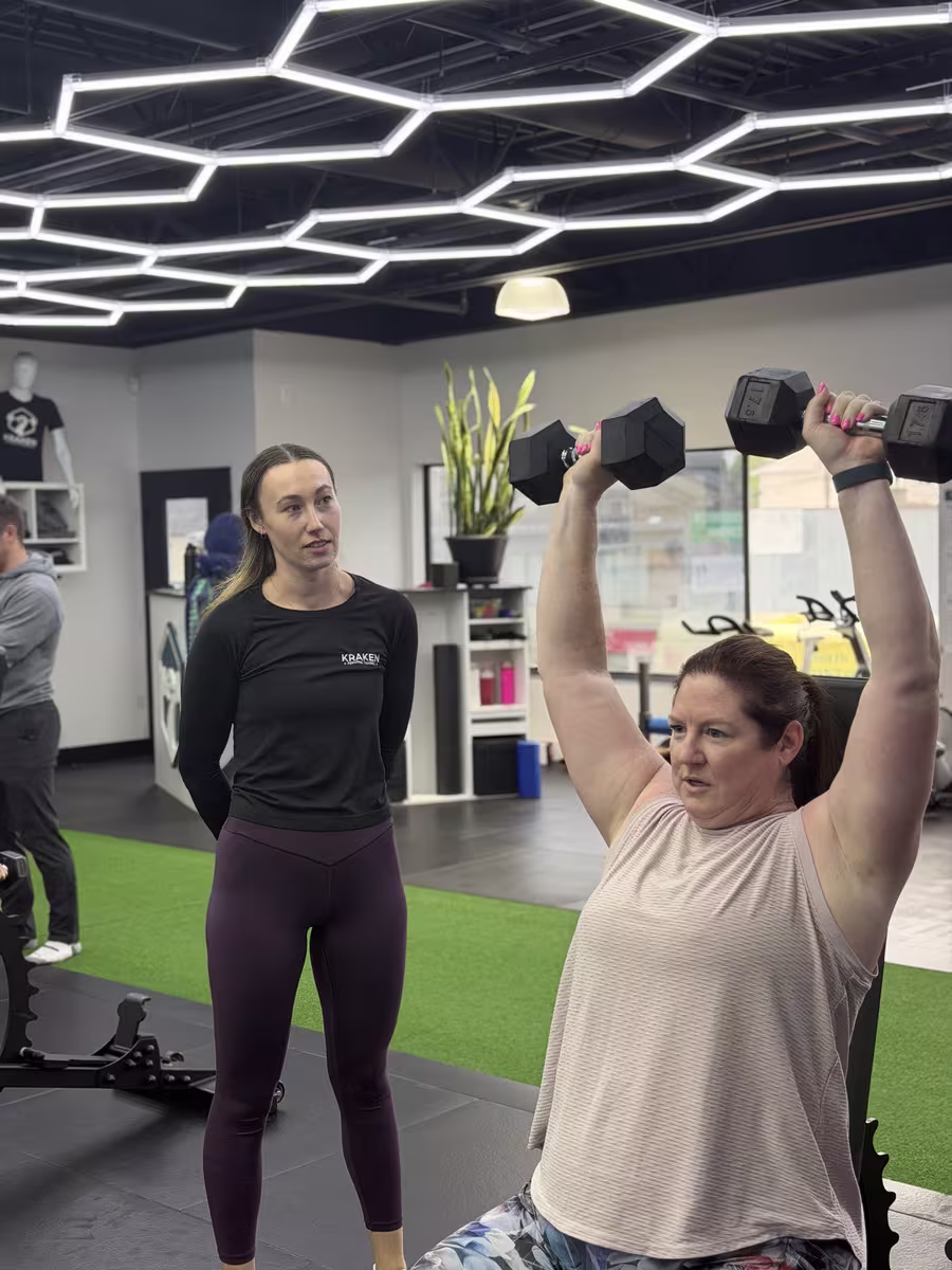 Justine coaching a member through an overhead press at Kraken