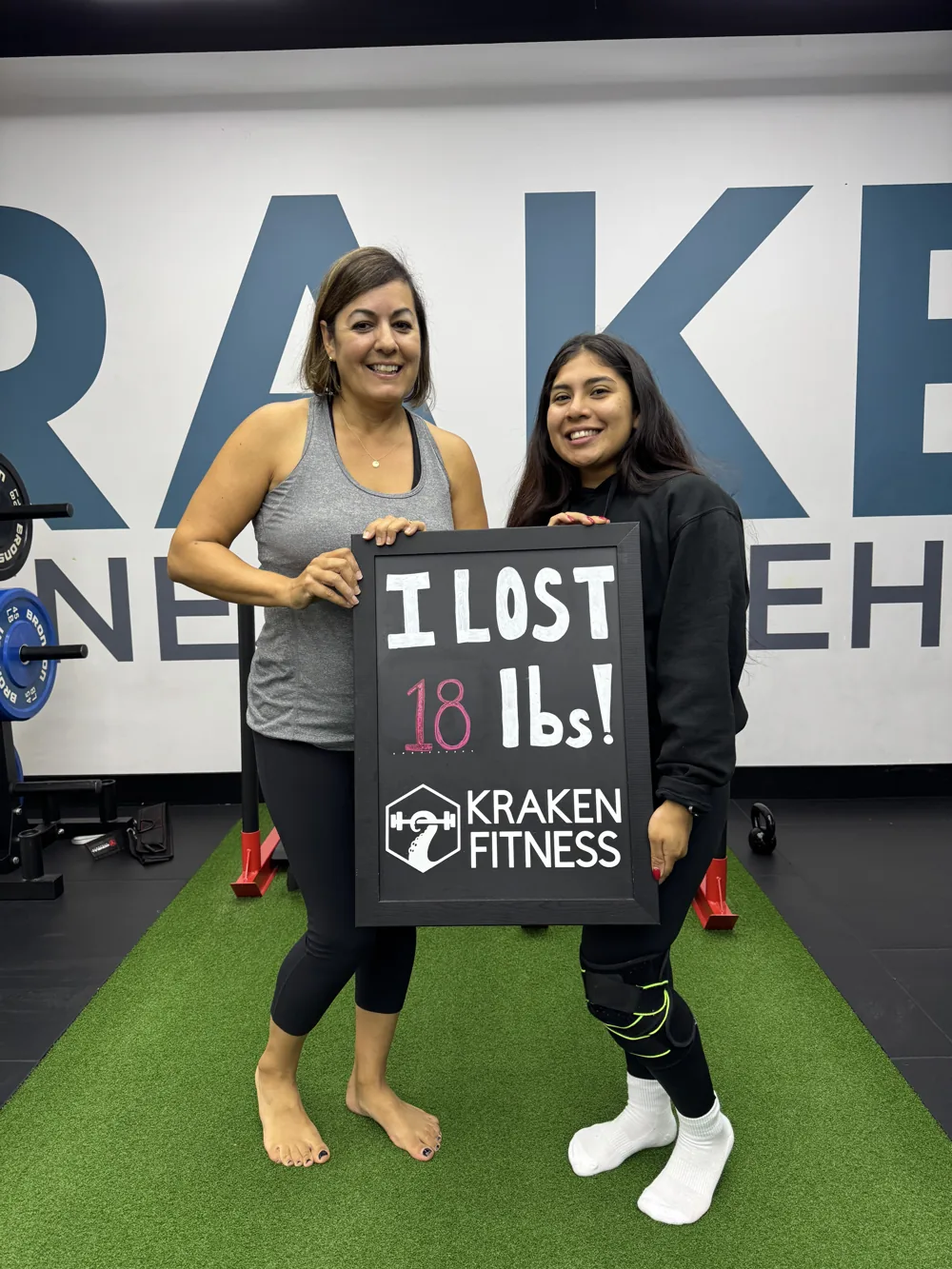 Cindy holding an I lost 18 lbs chalkboard at Kraken Fitness
