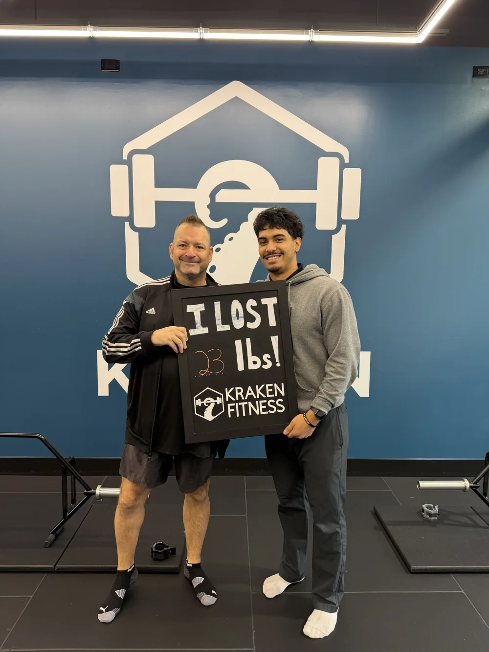 Lyle holding an I lost 23 lbs chalkboard at Kraken Fitness