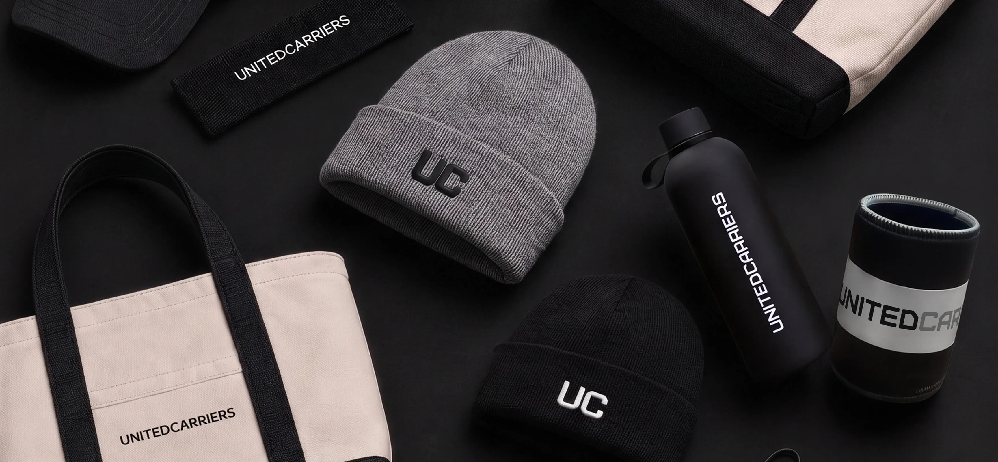 Black and gray beanies, tote bags, water bottle, and sleeve featuring United Carriers branding.