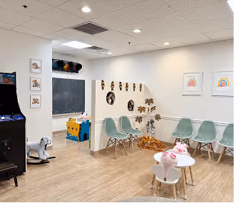 Children's playroom with pastel chairs, wall decorations, a small table with toys, and a rocking horse.