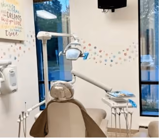 Dental exam chair with overhead light and tools in a bright office with colorful wall decals.