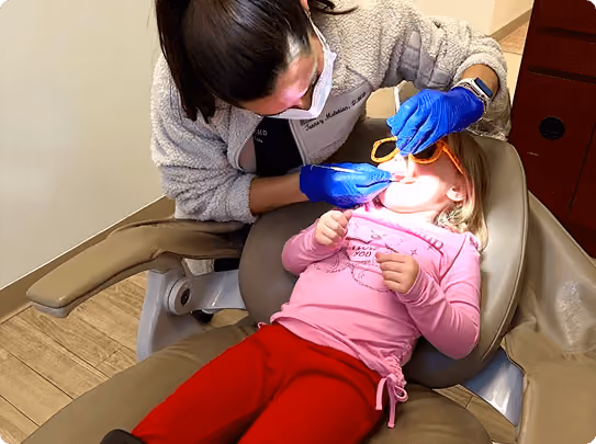 Smiling woman reclined in a dental chair, interacting with a dentist wearing blue gloves.