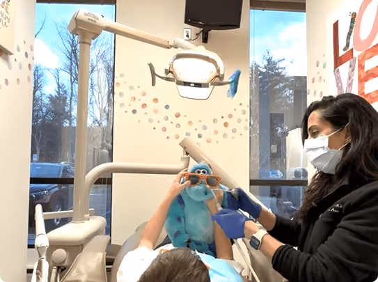 Smiling woman reclined in a dental chair, interacting with a dentist wearing blue gloves.