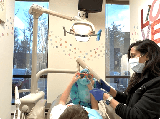 Smiling woman reclined in a dental chair, interacting with a dentist wearing blue gloves.
