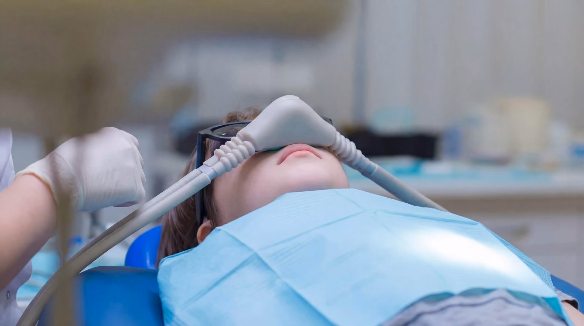 Smiling man sitting in a dental chair giving a thumbs-up in a bright dental office.