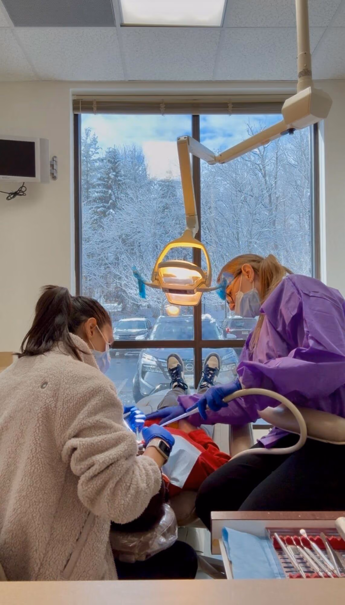 Smiling woman reclined in a dental chair, interacting with a dentist wearing blue gloves.