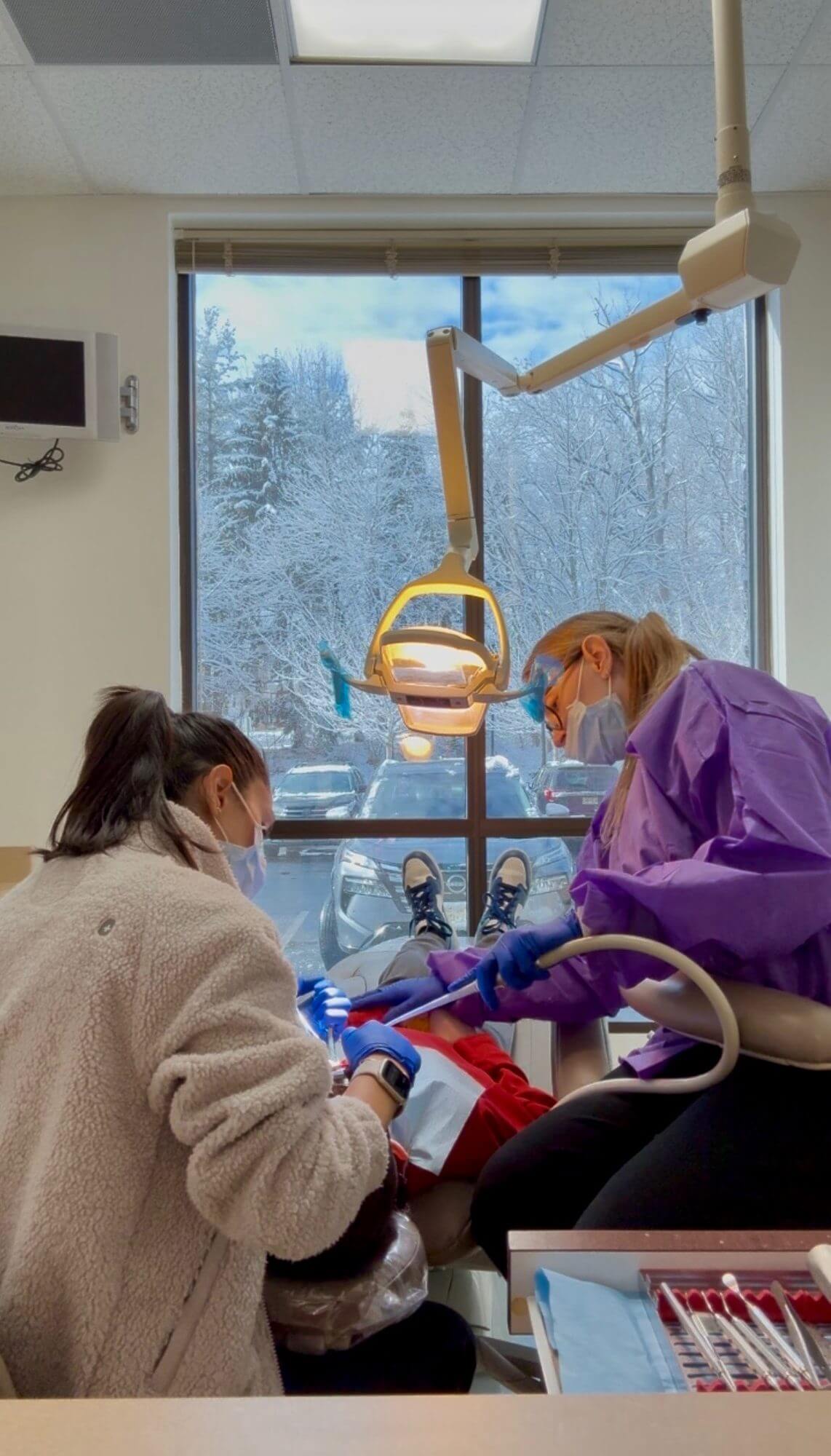 Smiling woman reclined in a dental chair, interacting with a dentist wearing blue gloves.