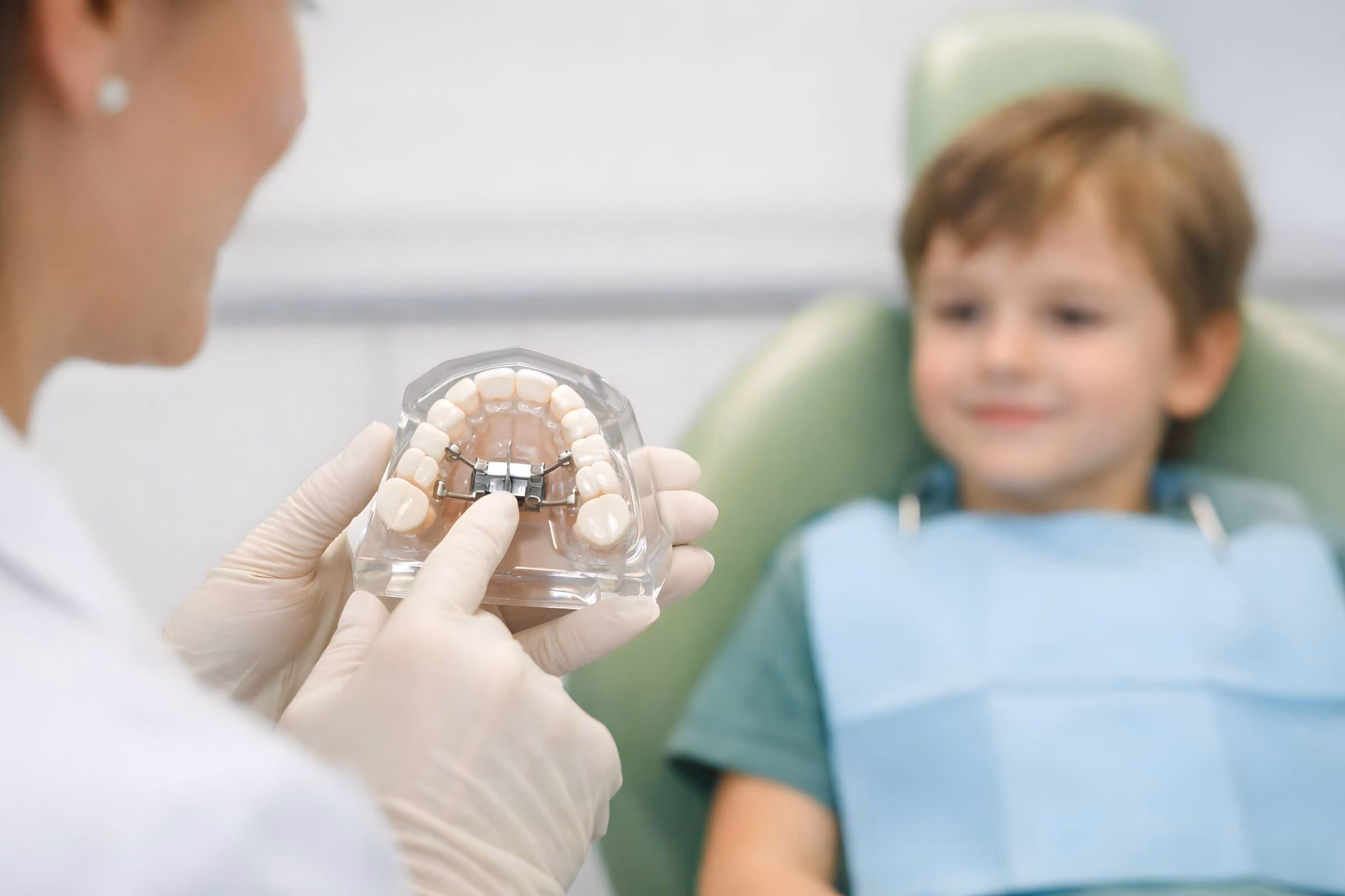 Smiling man sitting in a dental chair giving a thumbs-up in a bright dental office.