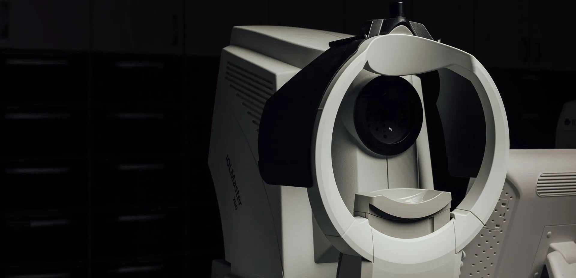 Close-up of a white and gray IOLMaster 700 ophthalmic device used for eye measurements in a dimly lit room.