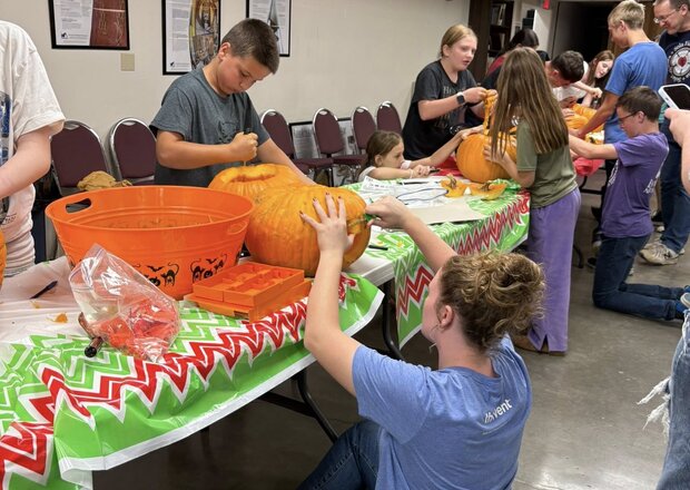The youth group at Trinity Lutheran Church in Paola, Kansas carve pumpkins on a green tablecloth during a youth event. 