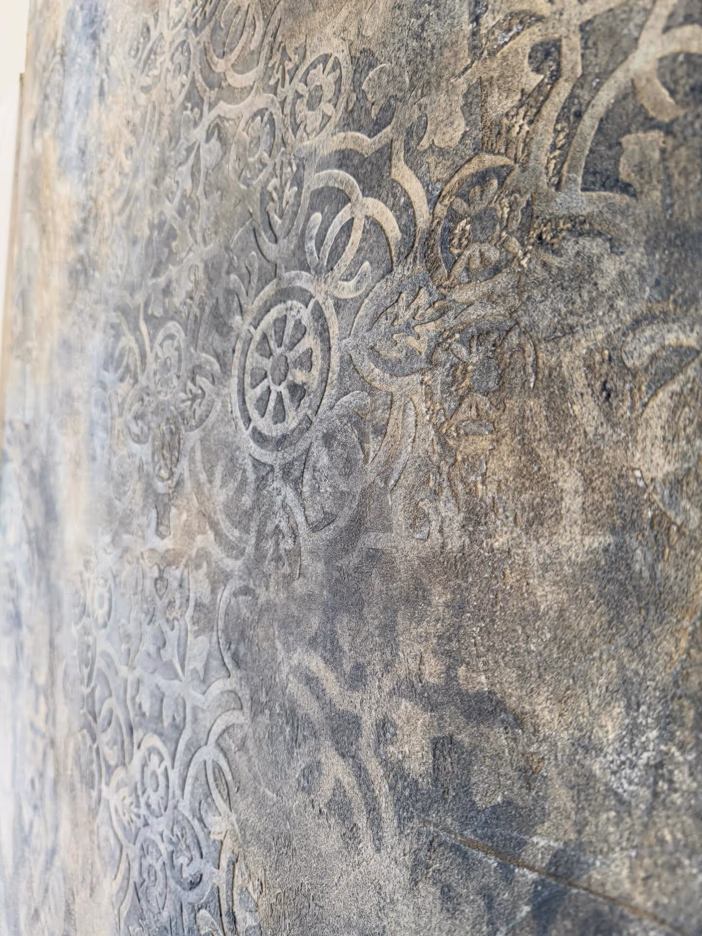 Mur texturé avec motifs floraux et géométriques sculptés visibles en relief.