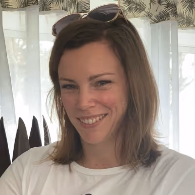 Portrait d'une femme souriante aux cheveux bruns avec des lunettes de soleil sur la tête.