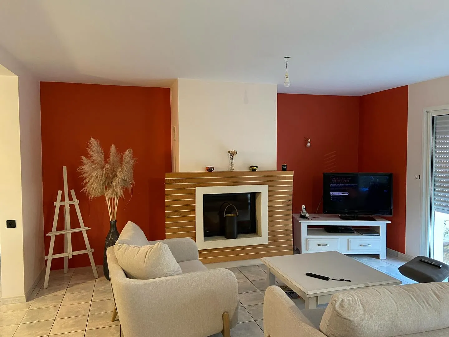 Salon avec murs orange, cheminée encadrée de bois, canapés beige, télévision et table basse blanche.