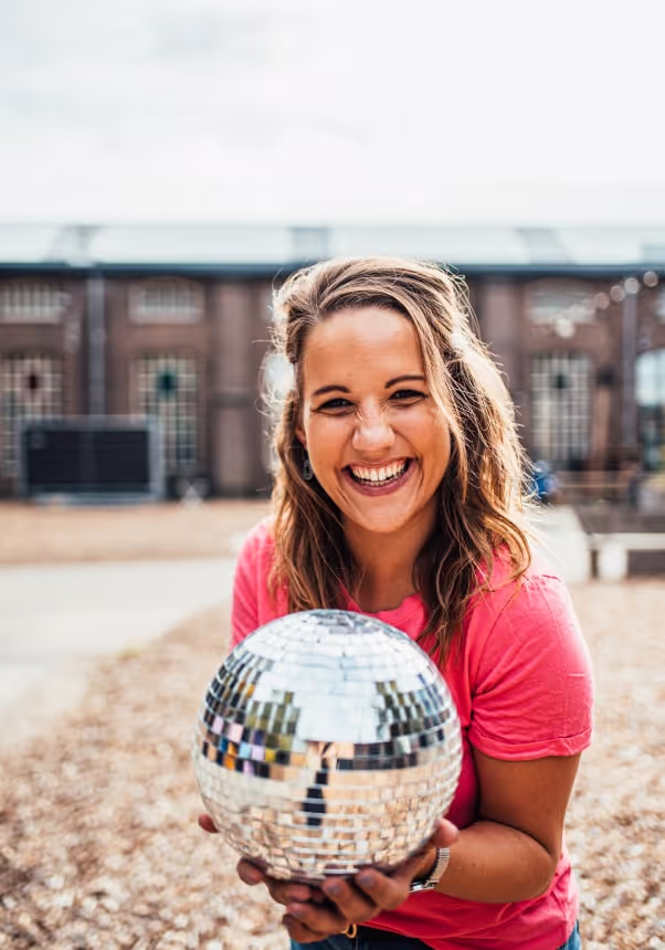 Karin met een roze shirt glimlacht terwijl ze een discobal vasthoudt.