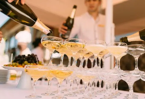 Mensen schenken champagne in een piramide van coupeglazen tijdens een feestelijke gelegenheid.