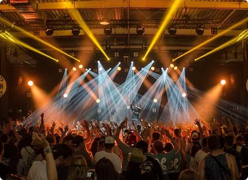 Drukke concertzaal met een menigte die geniet van een live optreden onder kleurrijke verlichting.