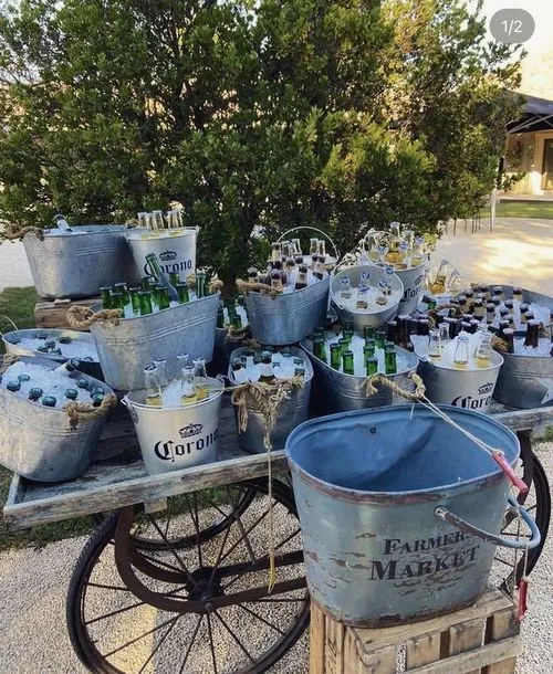 Diverse metalen emmers met flesjes bier op een houten kar, buiten met bomen op de achtergrond.