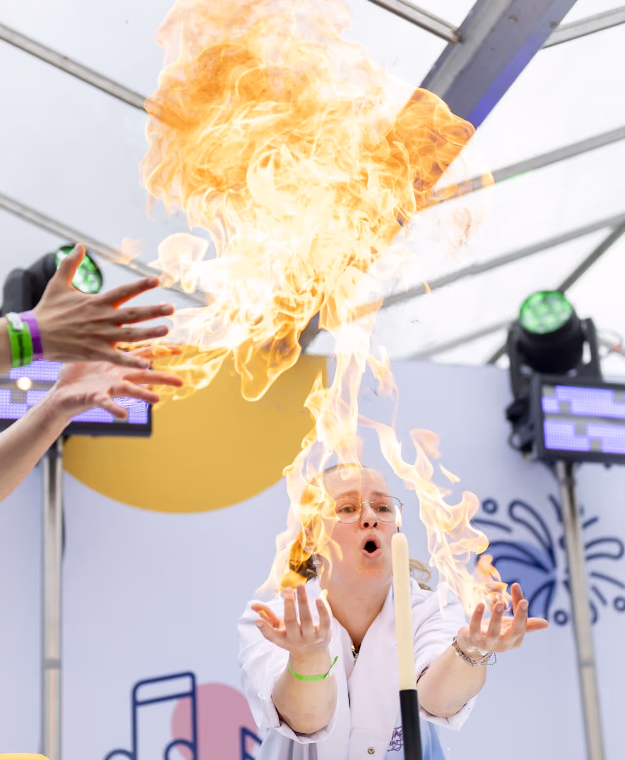 Een vrouw in een witte jas blaast vlammen uit haar handen tijdens een vuurshow.