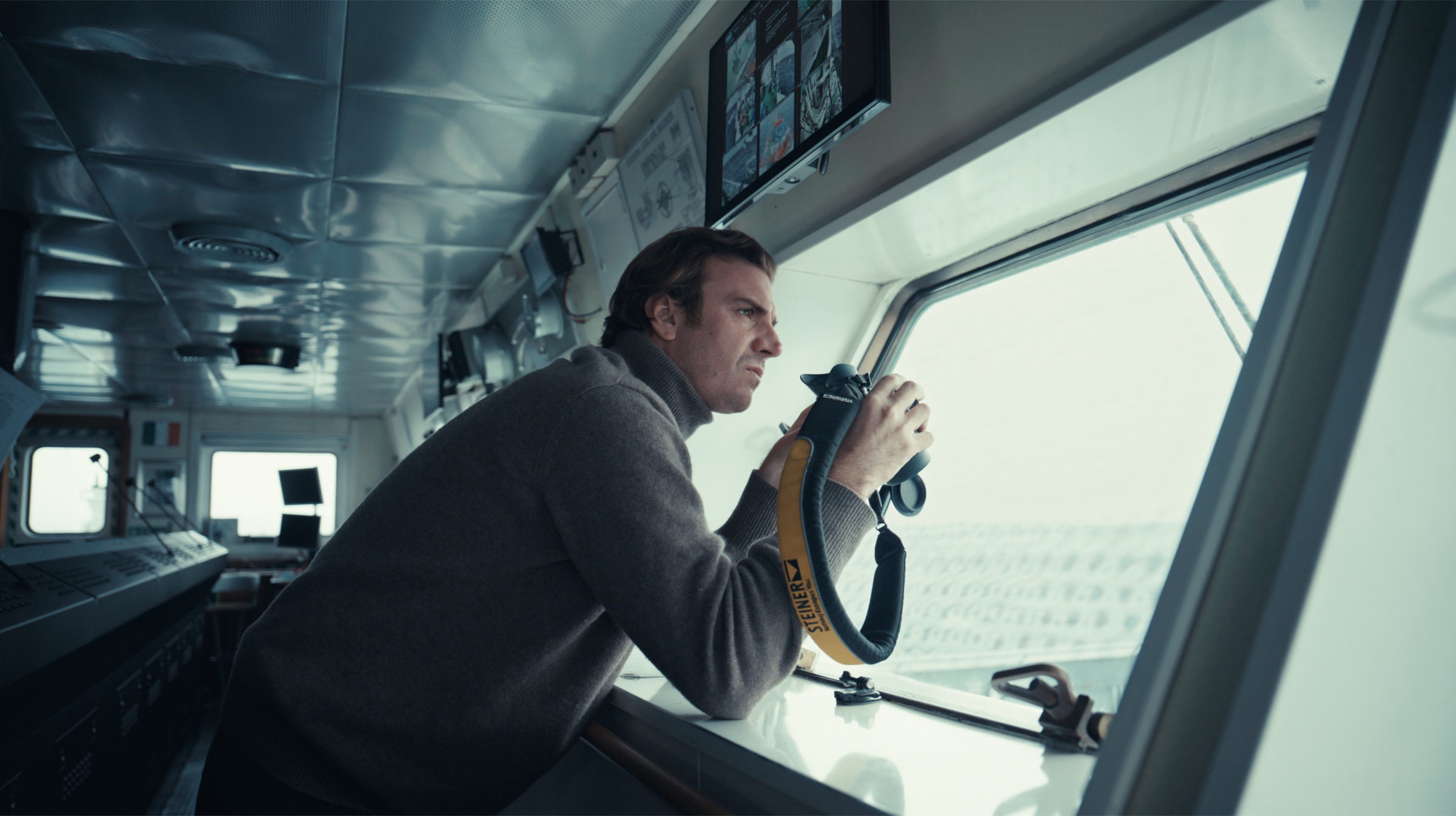 Niccolò Banfi watching the sea through binoculars from a ship's bridge