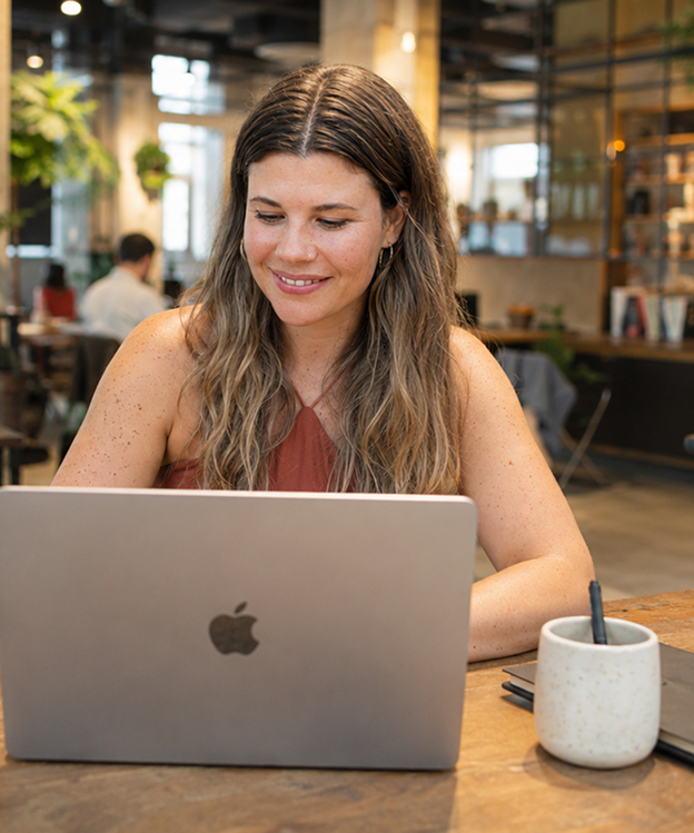 Woman with long hair working on a MacBook laptop at a wooden table in a café.