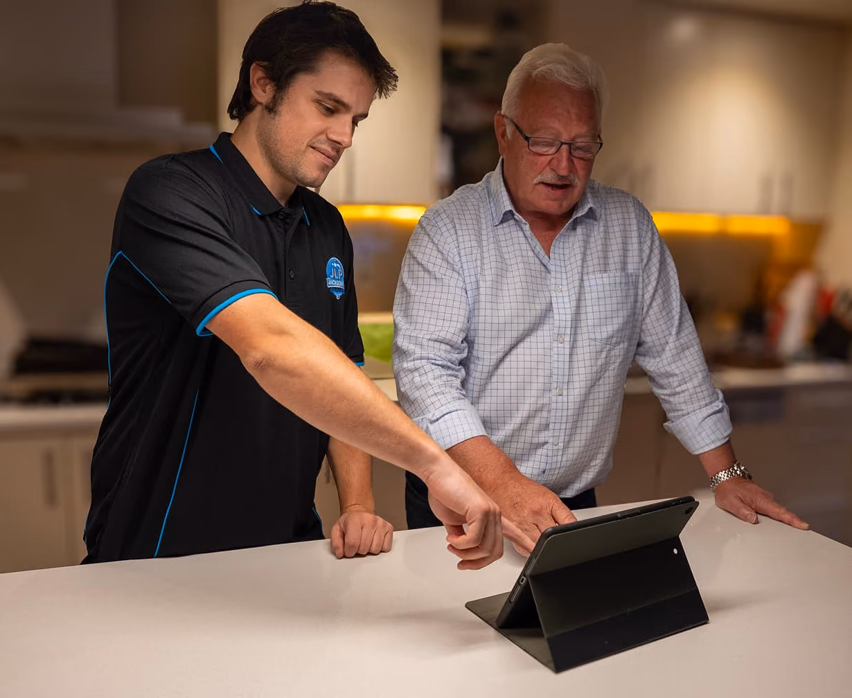 Younger man showing tablet screen to older man in a modern kitchen setting.