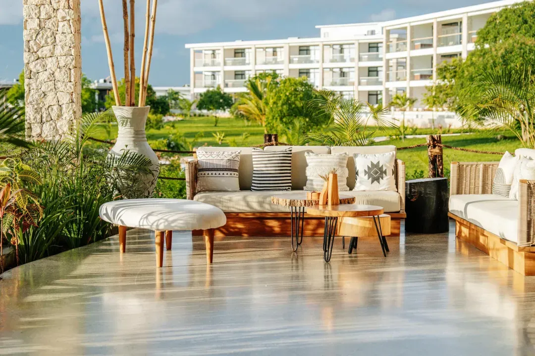 Outdoor seating area with cushioned sofas, patterned pillows, wooden tables, and large vase with bamboo sticks.