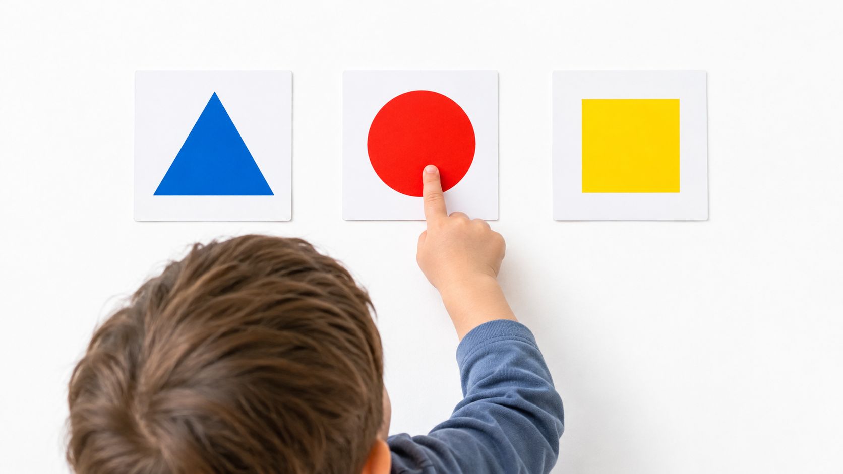 A young child pointing at a red circle on a wall card during a learning exercise.
